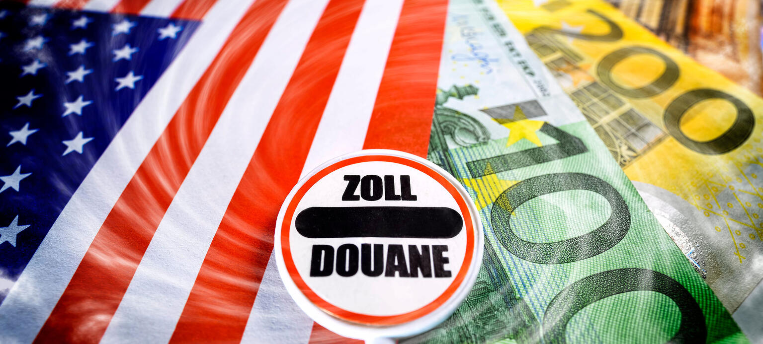 Zoll-Schild auf Fahne der USA und Euro-Geldscheine, US-Strafzoelle gegen Europa.