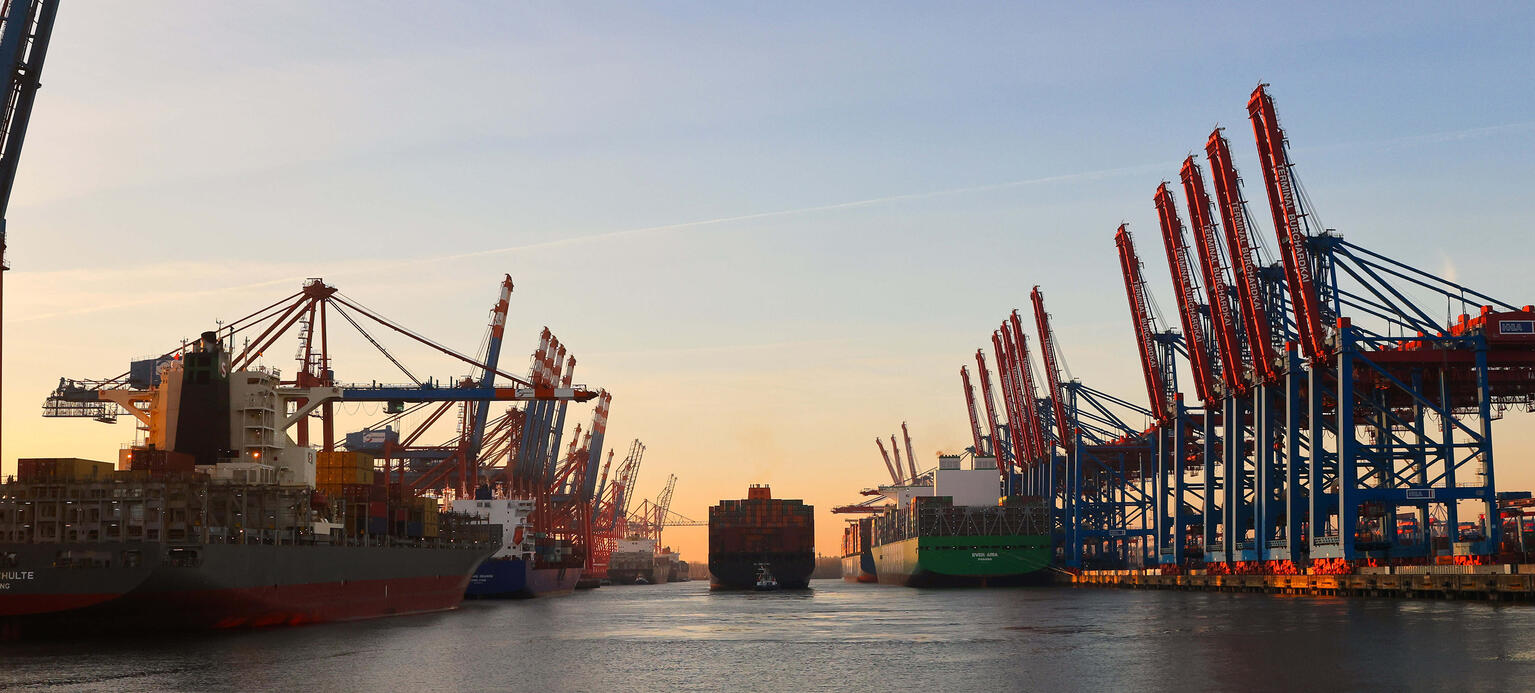 Ein voll belandenes Containerschiff verlässt einen Hafen während des Sonnenaufgangs.