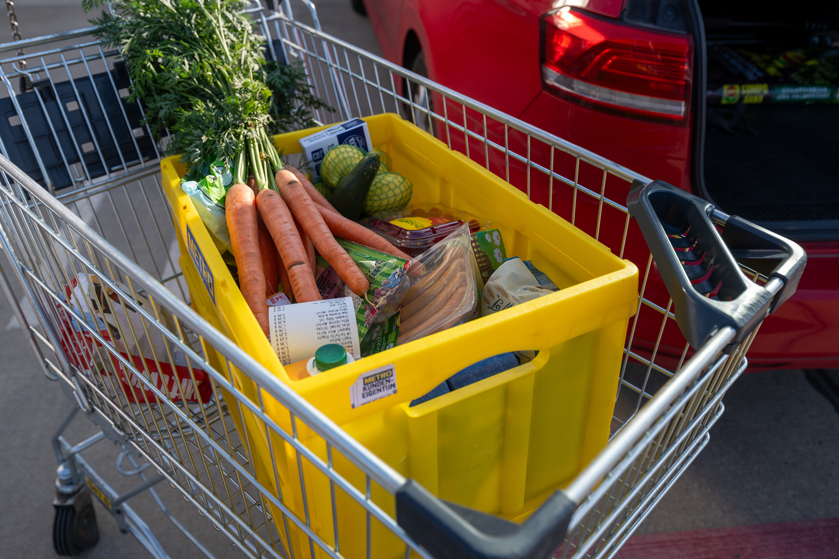 Eine Einkaufskiste mit Lebensmitteln steht in einem Wagen auf einem Parkplatz eines Supermarktes.